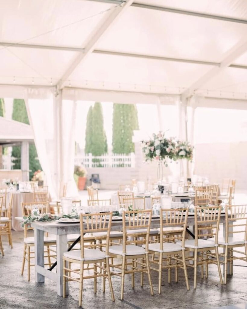 Long banquet tables and gold chairs set beneath the open-air pavilion