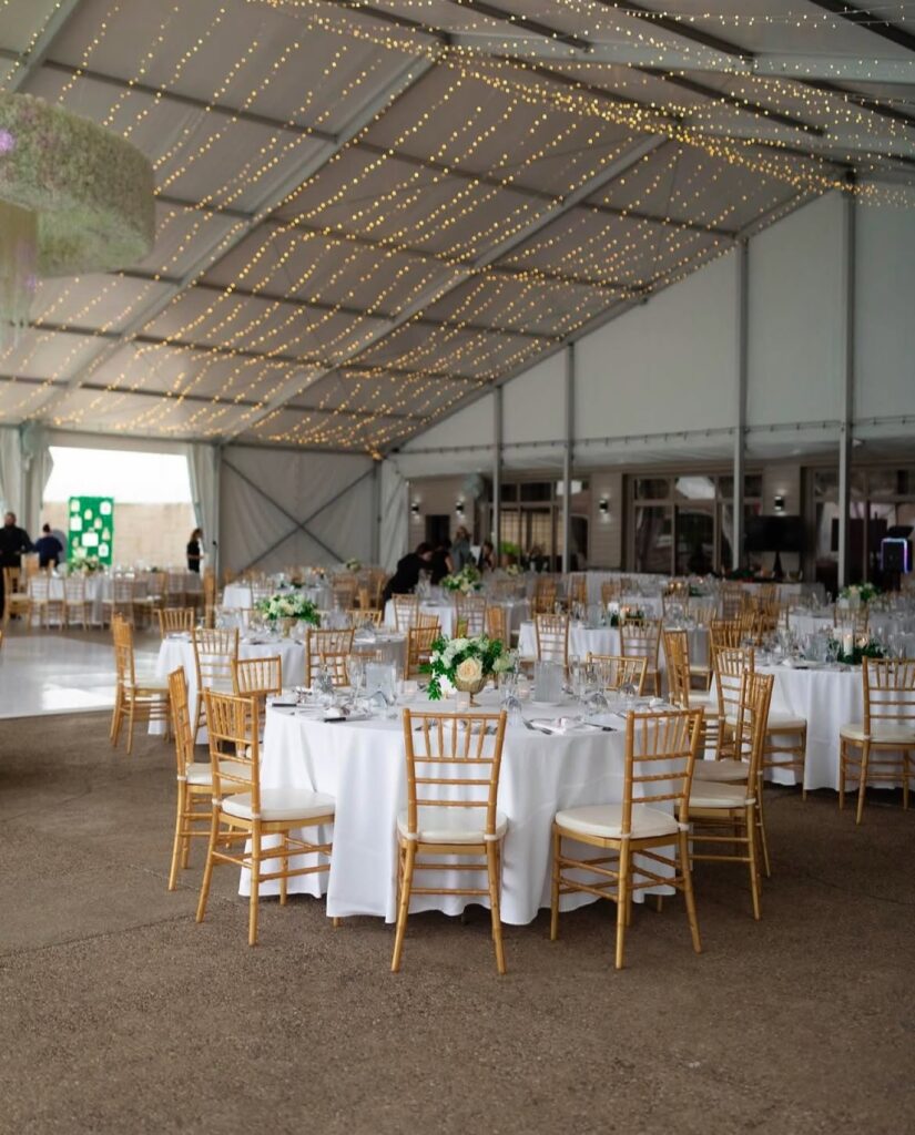 The pavilion under string lights with gold chiavari chairs and white linens
