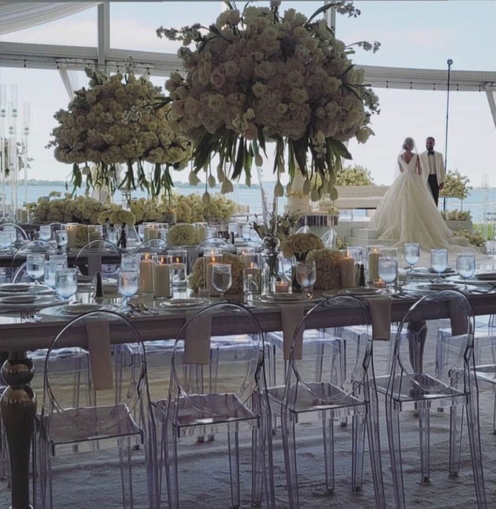 Tall greenery centerpieces above a long table of clear chairs
